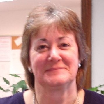 Woman smiling indoors with plants and bulletin board.